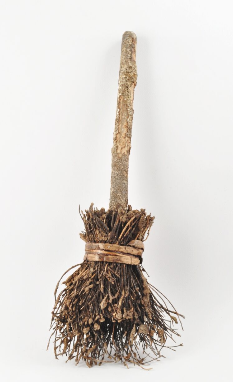Besen, Holz (Stiel: Tanne), im Querschnitt rechteckiger Stiel mit abgefasten Kanten, Stielende gerundet, Kopf aus dünnen Zweigen, ursprünglich mit dünnen Holzbändern gebunden (Spagat rezent).