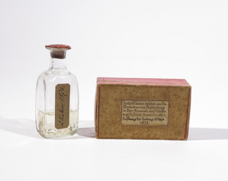 Hersteller unbekannt, Flasche mit Wasser aus der Fürstenbrunner Rohrleitung in Originalkarton, 1874–1875, Flasche: Glas, Siegelwachs, Wasser, Papier, Karton: Karton, 9,6 cm und 10 x 5,9 x 3,6 cm, Inv.-Nr. K 3542-49 © Salzburg Museum
