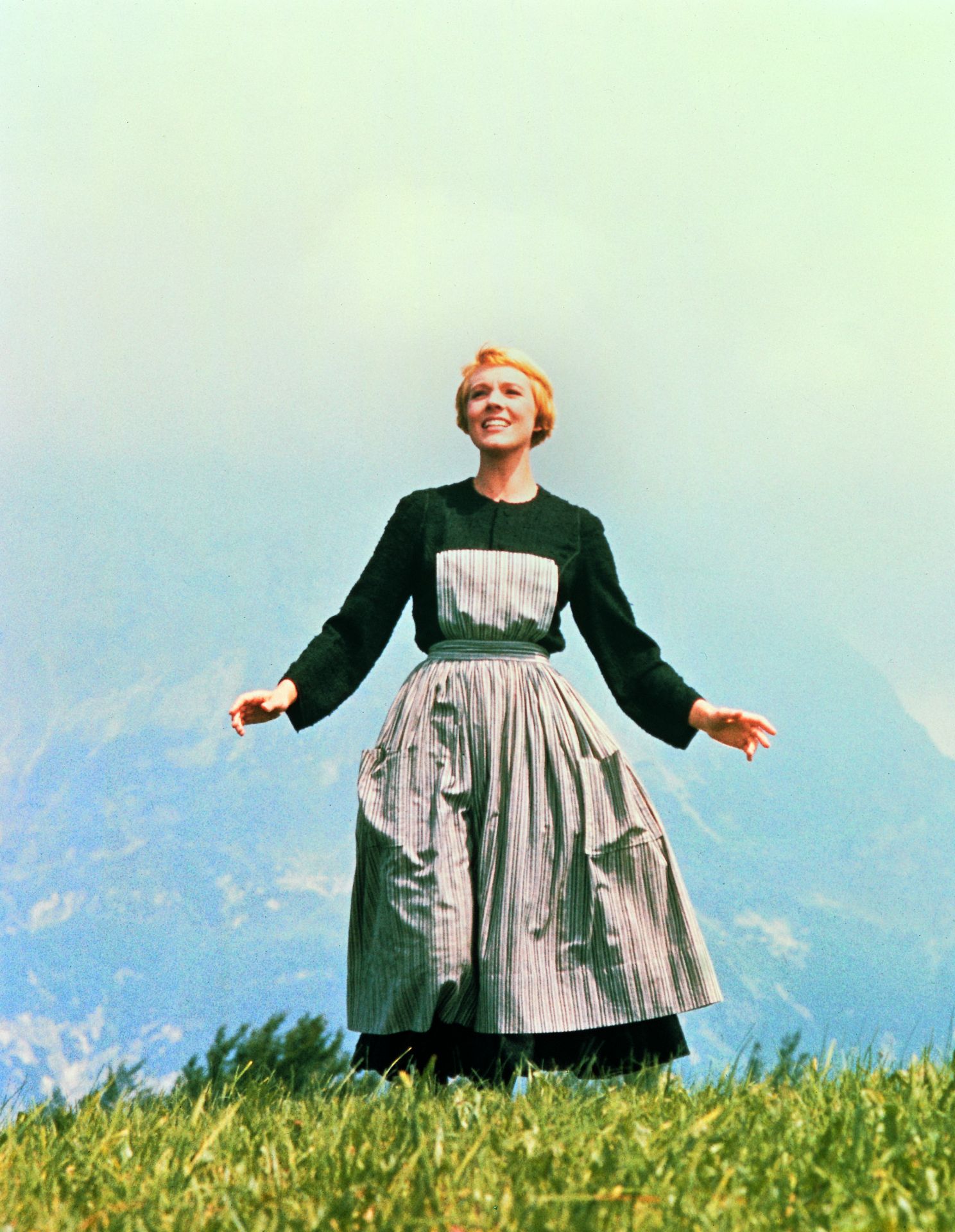 Julie Andrews steht singend mit ausgebreiteten Armen auf einer Wiese in der berühmten Filmszene aus „The Sound of Music“