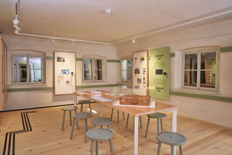 Ausstellungsraum zur Emigration der Familie von Trapp 1938 mit historischen Fotografien, Dokumenten, Hörstationen und einem Koffer.