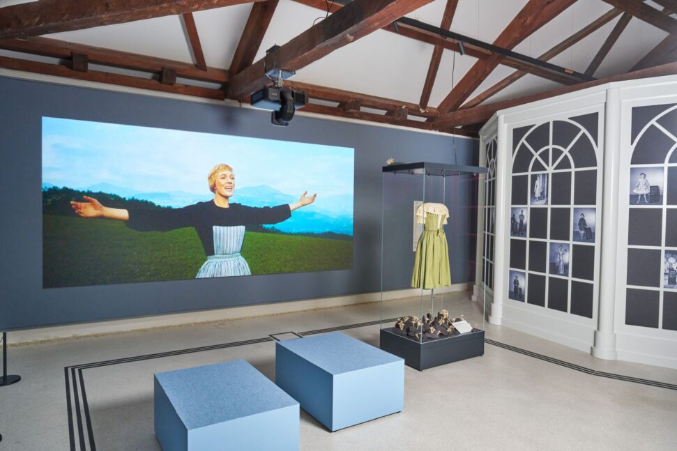 Ausstellungsraum zu „The Sound of Music“ mit großformatiger Filmprojektion, einem Kostüm in einer Glasvitrine und historischen Fotografien.