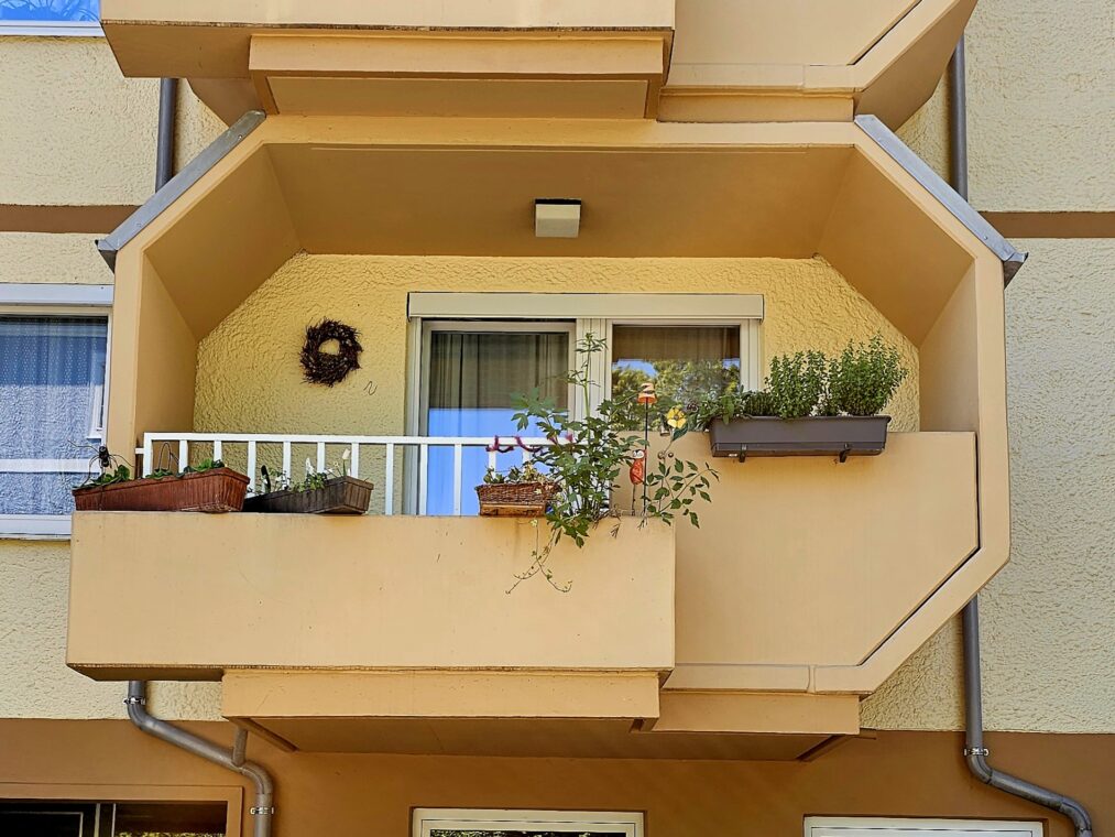 Detail eines Wohnbaus der Nachkriegszeit in Salzburg mit Balkon, Blumenkästen und Pflanzen.