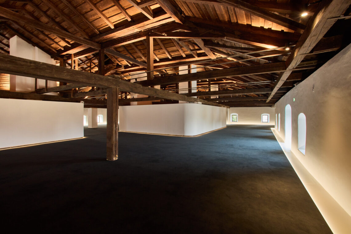 Großzügiger Veranstaltungs- und Ausstellungsraum im Kurt Zeller Forum des Keltenmuseums Hallein. Ein historischer Dachstuhl mit massiven Holzbalken überspannt den offenen Raum mit weißen Wänden, dunklem Boden und mehreren Rundbogenfenstern.