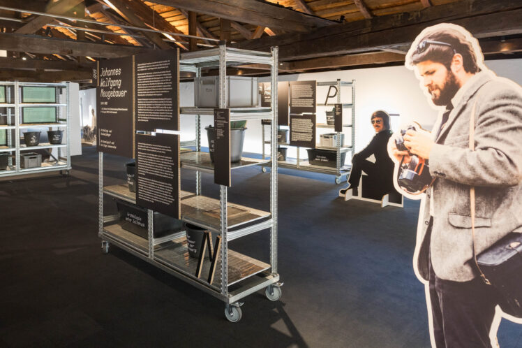 Ausstellungsansicht „Coole Kelten! Coole Forschung“ im Kurt Zeller Forum: Metallregale mit Fundobjekten und Texttafeln sowie lebensgroße Figurenaufsteller von Forschenden.