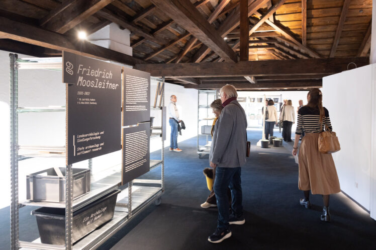 Ausstellungsansicht „Coole Kelten! Coole Forschung“ im Kurt Zeller Forum: Metallregale mit Fundobjekten und Texttafeln sowie lebensgroße Figurenaufsteller von Forschenden.